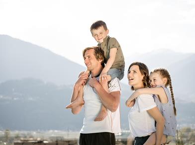 A happy family with two children enjoys the mountain view – the parents carry the children on their shoulders.