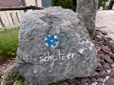 Large grey stone with a painted blue flower and the word “schatzer”