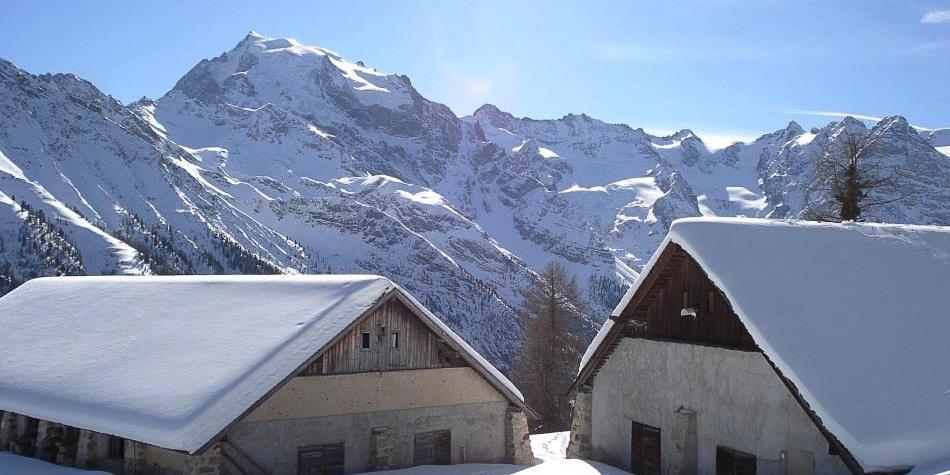 Two snow-covered mountain huts with a stunning Alpine backdrop under bright winter sun.