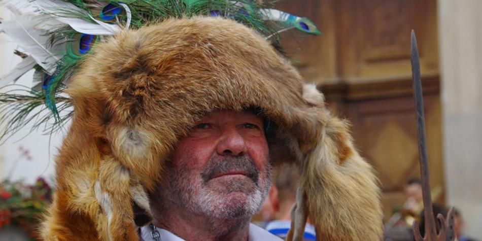 An older man wearing a traditional fur hat adorned with peacock feathers