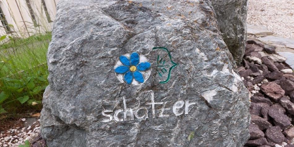 Large grey stone with a painted blue flower and the word “schatzer”