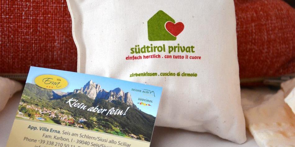 Cuscino di cirmolo con logo “südtirol privat” e biglietto da visita di Villa Erna su sfondo rosso.