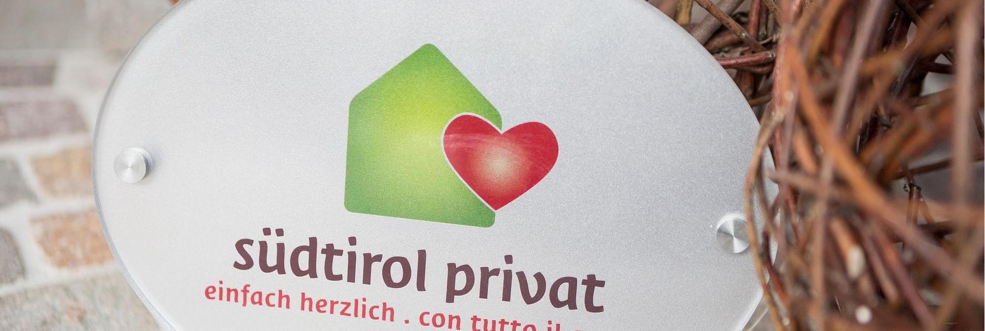 A sign with the logo of the private landlords and the text südtirol privat. einfach herzlich. con tutto il cuore