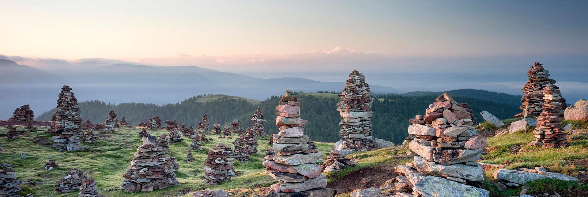 Cairns on an alpine meadow at sunrise with hills and mountains in the background.